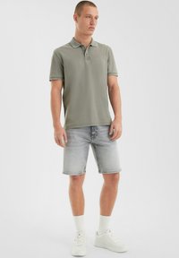 Grijze polo met korte mouwen, gecombineerd met lichte denim shorts. Witte sneakers en geribde sokken maken de outfit compleet. Schoon ontwerp, casual uitstraling.