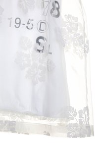 Bílá blůza s průsvitnou vrstvou, která má texturované květinové vzory. Na povrchu látky jsou viditelné černě tištěné číslice a písmena.