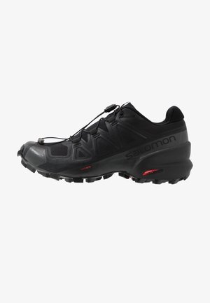 Zapatilla de trail running Salomon negra con suela rugosa, sistema de cordones rápidos y marca "contagrip" en el lateral.
