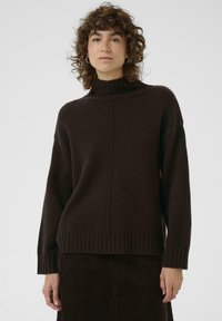 Un pull col roulé marron foncé en tricot doux, avec des poignets et un ourlet côtelés, un ajustement décontracté et des détails de couture verticale subtils.