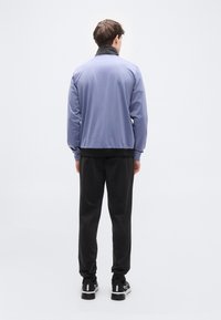 Μωβ-ανοιχτό μπουφάν με μαύρο γιακά, σε συνδυασμό με μαύρο παντελόνι και αθλητικά παπούτσια. Το μπουφάν έχει λεία υφή και άνετη εφαρμογή.