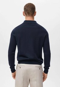 Polo pulover u tamnoplavoj boji od pletene tkanine s ovratnikom, prilagođenim dizajnom, rebrastim manžetama i rubom. Nosite s svijetlosmeškim hlačama. Glatka tekstura, elegantan oblik.