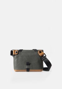 Green canvas crossbody bag with tan leather accents, adjustable black strap, and snap closures. Features a textured, matte finish.
