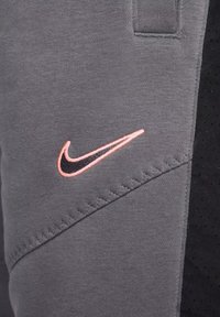 Pantaloni grigi in felpa con un accento nero. Presentano un orlo cucito e un logo Nike in rosa e nero. Realizzati in un tessuto morbido e testurizzato.