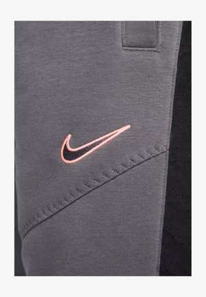 Pantaloni grigi in felpa con un accento nero. Presentano un orlo cucito e un logo Nike in rosa e nero. Realizzati in un tessuto morbido e testurizzato.