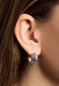 Silverfärgade hoops med spiraldesign och slät, glänsande yta, med räfflade detaljer längs den yttre kanten.