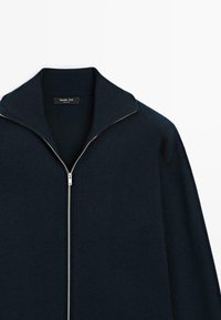 Cardigan blu navy con zipper, colletto a scialle a coste, texture a maglia liscia e dettaglio della zip in argento. L'etichetta riporta "Massimo Dutti."