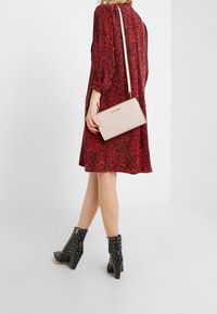 Abito rosso con stampa serpente, a maniche lunghe, abbinato a una borsa a tracolla rosa chiaro, stivaletti neri con borchie alla caviglia e una borsa dal design semplice.