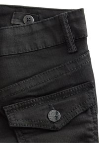 Svarta denimbyxor i närbild, med knäppning, sned framficka och kontrasterande sömmar. Slät textur med matt yta.