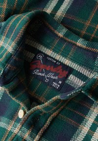 Camisa de franela a cuadros verde y azul marino con acentos en naranja y blanco, cuello con botones y una etiqueta roja con "Superdry Ranch Wear".