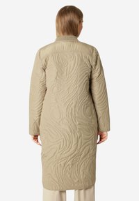Abrigo largo acolchado beige con patrones en espiral texturizados, que presenta un cuello alto y mangas largas, diseñado para proporcionar calidez y protección.