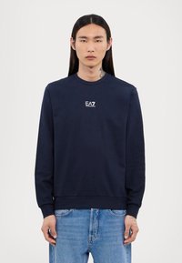 Tums zilgans džemperis no kokvilnas maisījuma ar garām piedurknēm, apaļu apkakli un mazu baldu logo uz krūtīm. Raksturīgas ribotas piedurkņu un apakšmalas.