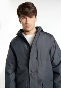 Giacca a hood grigia con chiusura a zip e bottoni automatici, tasche frontali, una texture liscia e una finitura leggermente lucida.