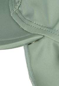 Grüne Stoffmütze mit glatter Textur, ausgestattet mit genähten Details und einem gebogenen Schirm, entworfen für Komfort und Sonnenschutz.