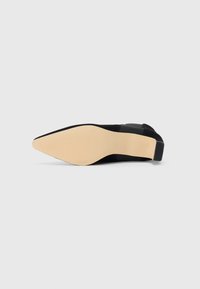 Pantof de dama cu toc înalt, de culoare neagră, cu vârf ascuțit și suprafață texturată. Talpa este de culoare bej, cu un finisaj neted și ușoare striații pentru aderență.