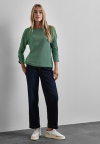 Groene lange mouwen overhemd met een textuurpatroon, gecombineerd met donkerblauwe wijde jeans en witte sneakers met beige accenten.