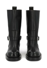 Botas de cuero negro hasta la rodilla con una textura suave, punteras redondeadas, hebillas plateadas y suelas planas, con una lengüeta en la parte posterior.