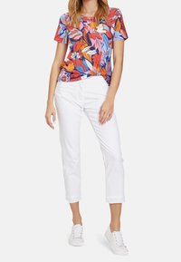 Blommig mönstrad kortärmad topp i blått, orange och rosa; tillsammans med vita capribyxor och vita sneakers.