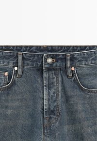 Dark blue denim jeans featuring a traditional button fly, copper rivets, and subtle whiskering near the waistband and pockets.
