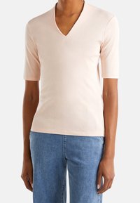 Ljusrosa kortärmad V-ringad skjorta i mjukt material; har en figursydd design och rak fåll; kombinerad med blå denimjeans.