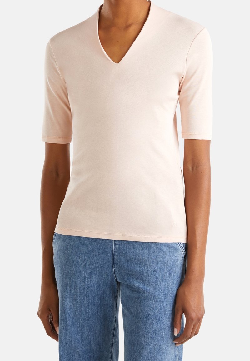 Ljusrosa kortärmad V-ringad skjorta i mjukt material; har en figursydd design och rak fåll; kombinerad med blå denimjeans.