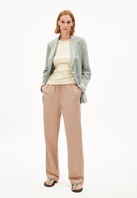Grau gestreifter Blazer über einem hellgelben Oberteil, kombiniert mit lockeren, beigen Hosen. Schwarze Flip-Flops mit grünen Riemen runden den Look ab.