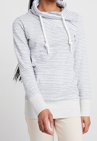 Sudadera ligera a rayas en blanco y azul marino, con cuello de cisne y cordones. Presenta mangas largas y puños acanalados para mayor comodidad.