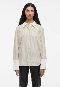 Gestreepte button-up shirt in crème met lichte roze en beige lijnen, met een witte kraag en brede witte manchet. Zacht materiaal, losse pasvorm.