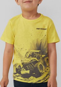 Gelbes Baumwoll-T-Shirt mit einem schwarzen Grafikdruck eines Geländewagens und dem Text "ZEIT ZU GENIESSEN", ergänzt durch Farbspritzer-Designakzente.