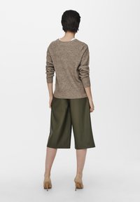 Beige gestrickter Pullover mit lockerer Passform, kombiniert mit olivgrünen Culotte-Hosen. Schuhe in einem hellbraunen Farbton runden das Outfit ab.