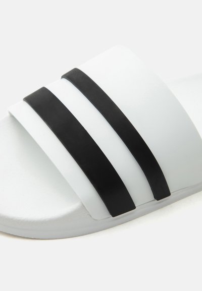 Sandale blanche à talon plat avec deux larges brides horizontales noires sur le dessus.