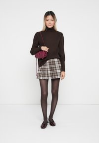 Smeđa rebrasta turtleneck dukserica, karirana mini suknja u bež/zelenoj boji, crne neprozirne čarape, burgundska torba preko ramena i sjajne tamne cipele.