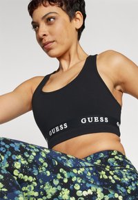 Sujetador deportivo negro con banda de logo, combinado con leggings de patrón floral azul y verde, que muestran un diseño ajustado y una tela elástica.