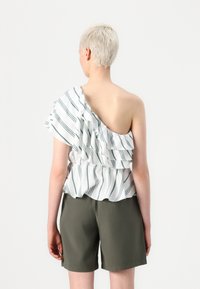 Top alb cu volane, cu dungi verzi, design pe umărul unic. Asortat cu pantaloni scurți de culoare verde măsliniu, material casual și croială relaxată.