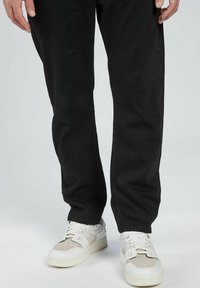 Svarta bomullshängselbyxor med en lös passform, tillsammans med vita sneakers med beige detaljer och en texturerad paneldesign.