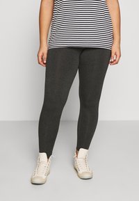 Mörkgrå leggings med en slät textur, kombinerat med en svartvit randig topp. Vita hög-top skor fulländar outfiten.