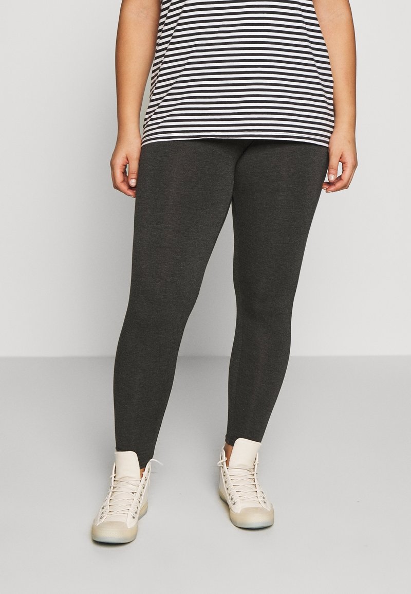 Mörkgrå leggings med en slät textur, kombinerat med en svartvit randig topp. Vita hög-top skor fulländar outfiten.