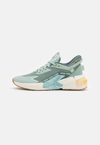 Light green Puma sneaker with textured mesh, light blue heel support, multicolor heel detail, and gum rubber outsole, side view on white background.