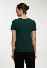 Ciemnozielona koszulka z krótkim rękawem, okrągłym dekoltem, wykonana z miękkiego materiału. Gładka tekstura, dopasowany krój oraz subtelne wykończenie u dołu.