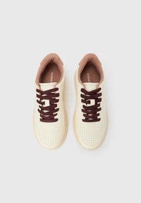 Paire de baskets couleur crème avec des lacets marron foncé et une doublure intérieure marron clair, vues de dessus sur fond blanc.