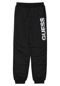 Czarne ocieplane dresy z elastycznym pasem, bocznymi kieszeniami, ściągaczami przy kostkach oraz białym logo "GUESS" na lewej nodze. Gładka faktura.