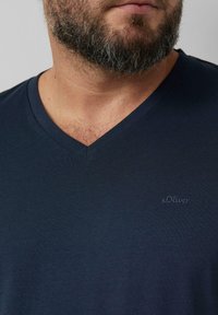 Marineblaues V-Ausschnitt-T-Shirt aus weichem Stoff, mit einem dezenten s.Oliver-Logo auf der Brust bestickt. Glatte Textur und modernes Design.