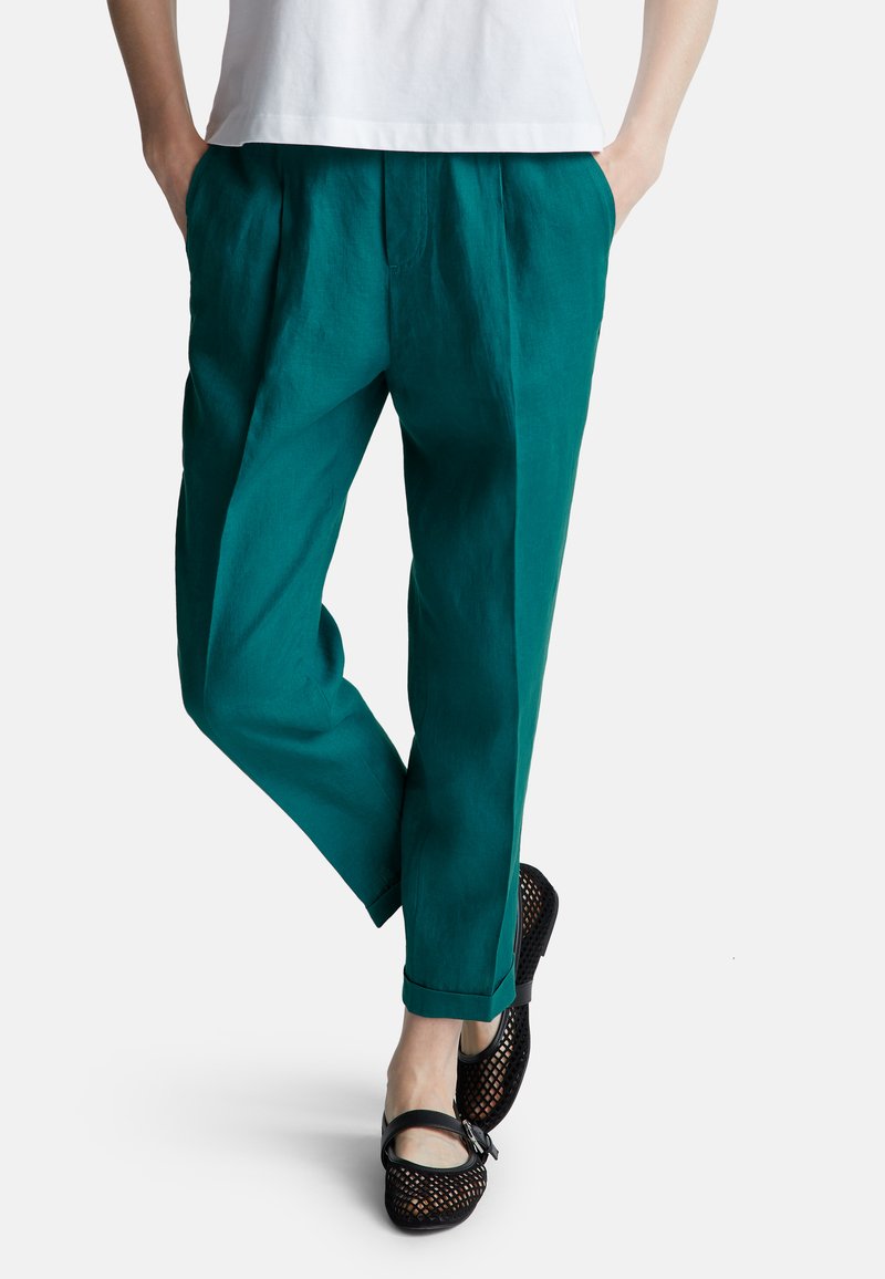 Turkusowe lniane spodnie o luźnym kroju, z fałdami i podwiniętymi mankietami, w zestawieniu z czarnymi plecionymi butami.