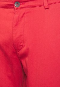 Pantalon rouge en tissu lisse. Présente une coupe droite, un devant plat, des poches latérales et une fermeture par bouton avec des coutures contrastantes.