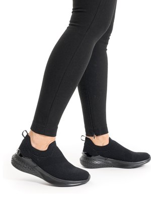 Zwarte sportieve schoenen met een ademende gebreide bovenkant, een gestructureerde zool en een glad zwart accent bij de hiel. Draagt met zwarte legging.