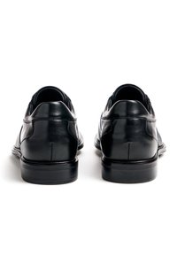Schwarze Leder-Dressschuhe mit glatter Oberfläche, abgerundetem Zehenbereich und niedrigem Absatz. Sie verfügen über gestickte Details und ein elegantes, minimalistisches Design.