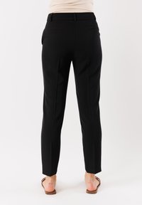 Pantaloni neri su misura con gamba dritta, realizzati in un tessuto liscio, dotati di passanti per cintura e tasche. L'orlo è a taglio dritto e arriva alla caviglia.