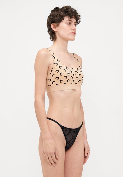Beež bralette mustritega musta poolkuud, mida on kombineeritud musta läbipaistva stringiga, millel on ringikujulised mustrid, mõlemad pehmetes materjalides.