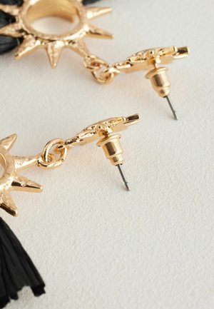 Cercei aurii cu un design în formă de raze de soare, ornamentați cu ciucuri negri. Prindere cu ac pin și finisaj texturat.