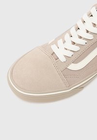 Baskets beiges en daim et toile avec lacets blancs, bande latérale blanche et semelle en caoutchouc sur fond clair.